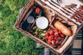 Picnic set with fruit, cheese, honey, strawberries, grapes, baguette, wine, wicker basket for picnic on plaid over green Royalty Free Stock Photo