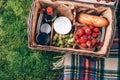 Picnic set with fruit, cheese, honey, strawberries, grapes, baguette, wine, wicker basket for picnic on plaid over green Royalty Free Stock Photo