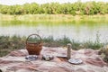 Picnic set, metal Cutlery, thermos, plates tea cups. brown plaid and napkin from the lake in the background. green grass. Sunny su