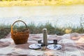 Picnic set, metal Cutlery, thermos, plates tea cups. brown plaid and napkin from the lake in the background. green grass. Sunny su