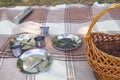 Picnic set, three persons. metal Cutlery, thermos, plates, tea cups. brown plaid and napkin from the lake in the background. green