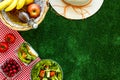 Picnic in summer with products, sandwich, salad, fruits, drink and hat on green grass texture background top view mockup