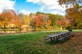 Picnic table and BBQ on a meadow covered in falle leaves alongside a river Royalty Free Stock Photo