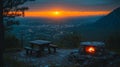 A picnic table and a stone fire pit with flames on a mountaintop overlooking a city at sunset Royalty Free Stock Photo