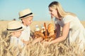 Mother gives children a basket with fresh bread and milk. A picnic on a wheat field. Royalty Free Stock Photo