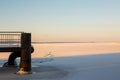 Pictorial winter landscape of frozen river lit by red sun and endless cloudy sky with part of snow-covered river pier Royalty Free Stock Photo