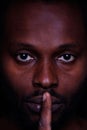 A picture of an African man looking at you with a finger across his lips