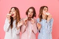 Picture of amazing three women friends wearing leisure clothings eating donuts and having fun at pajamas party, isolated over pin