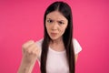 Picture of angry dissatisfied Asian woman clenches fist with displeasure, keeps lips folded, makes outraged face expression, wears