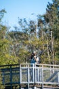 A picture of an Asian man taking a photo from atop a viewing tower in a park.