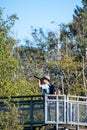 A picture of an Asian man taking a photo from atop a viewing tower in a park.