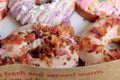 Picture of assorted donuts in a box with Bacon topping, pink glazed and sprinkles donuts.
