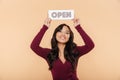 Picture of beautiful woman in maroon dress holding sign with word open over head being friendly on peach background