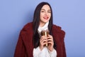 Picture of beautiful young brunette woman wearing winter jacket and holding thermo mug with coffee or tea in studio,  over Royalty Free Stock Photo