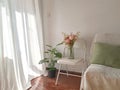 Picture captures a cozy bedroom, featuring two vibrant vases of flowers and a bright white chair