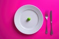 The picture captures a whimsical scene where a lone green pea takes center stage on a pristine white plate, set against