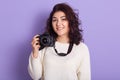 Picture of charming magnetic young female with curly black hair, holding photo camera, taking photos, smiling sincerely, wearing