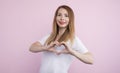 Picture of cheerful beautiful charismatic female looking directly at camera, making gesture, showing shape of heart with