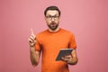 Picture of cheerful young bearded man standing near copyspace over pink wall background isolated. Using tablet computer pointing Royalty Free Stock Photo