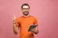 Picture of cheerful young bearded man standing near copyspace over pink wall background isolated. Using tablet computer pointing Royalty Free Stock Photo