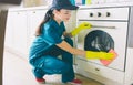 A picture of cleaner sitting in squad position and washing stove. She uses orange rag. Girl cleans very good. She is a