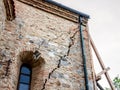 Cracked facadeof a stone wall of an old and decaying building, heavily needing renovation to avoid complete collapse