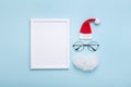 Picture frame, santa hat, beard and glasses on blue background top view. Creative christmas mockup. Greeting card or invitation.