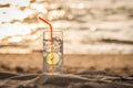 Glass of Gin Tonic with straw and lime slice on the beach, at sunset. Long Beach, Ko Lanta, Thailand.