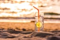 Glass of Gin Tonic with straw and lime slice on the beach, at sunset. Long Beach, Ko Lanta, Thailand.