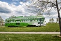 Green trolley driving past a park