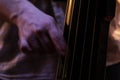 Selective blur on the hands of a musician touching the strings of a contrabass cello, playing pizzicato, in a dark environment, Royalty Free Stock Photo