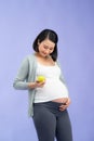 Picture of happy young pregnant asian woman standing isolated over purple background. Looking camera holding apple