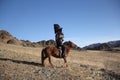 Picture of a horserider with a black eagle on a brown horse surrounded by rocks under a blue sky