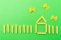 Picture with house made from penne type of italian pasta and farfalle butterflies on green background. Home made italian pasta Royalty Free Stock Photo