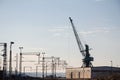 Industrial landscape at sunst, with an electrified railway line and its tracks, next to a heavy loading crane