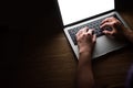 Picture light from the laptop screen. People are sitting in a dark room using a laptop on a wooden table