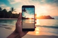 Picture of mans hand holding smartphone with beautiful picture on screen. Tropical beach with palms white sand and turquose water Royalty Free Stock Photo