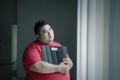 Pensive obese man holding a scale near the window