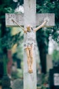 Picture of old wooden or stone cross with figure of crucified Jesus Christ. Memory on grave or cementary. Green trees on Royalty Free Stock Photo
