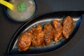 Picture of pan fried chicken stuffed momo served in a black plate along with chicken soup in a bowl on black background