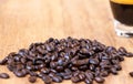 Picture of a pile of dark brown roasted organic coffee bean on a wooden table with a soft focus on a cup of coffee. Selective
