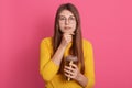 Picture of serious thoughtful young model holding mug with drink, looking directly at camera, having pensive facial expression, Royalty Free Stock Photo