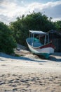 The picture shows a small fishing boat on a beach in front of a wooden hut and green bushes on a sunny day Royalty Free Stock Photo