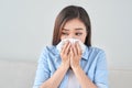 Picture of a sick young lady sitting on the couch and blowing her runny nose