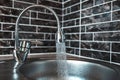 Picture of silver coloured opened faucet, with pouring water in the sink, in the kitchen area. On the background of dark brick Royalty Free Stock Photo