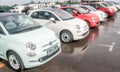 Picture of small and beutiful fiat cars standing outside on parking lot. There are red and white cars. Asphalt is wet