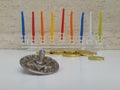 A glass Hannukiah filled with colourful candles on a white table with some scattered chocholate coins and a silver dreidel Royalty Free Stock Photo