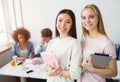 A picture of two beautiful asian girls standing and smiling. Brunette holds a pink notebook while the blonde girl has a