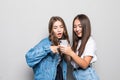 Picture of two smiling ladies friends looking aside using mobile phone. standing isolated over gray background Royalty Free Stock Photo