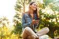 Woman student sitting in the park using mobile phone listening music. Royalty Free Stock Photo